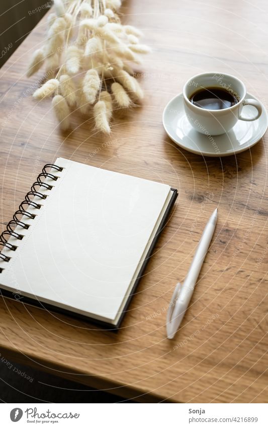 Ein leerer Notizblock, ein Kugelschreiber und eine Tasse Kaffee auf einem Holztisch Notizbuch zuhause Papier Tischplatte feminin Tagebuch Gedeckte Farben