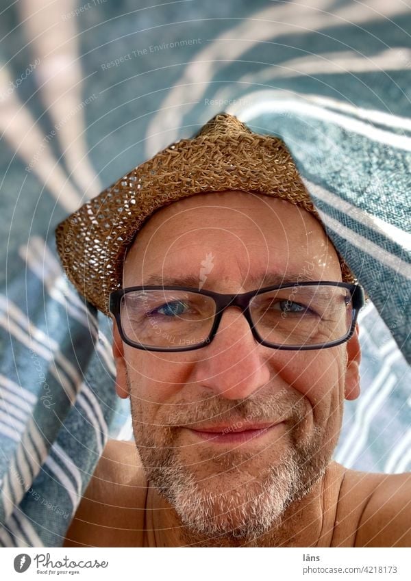 Strandleben unterm Strandtuch Mann Porträt Zufriedenheit Erwachsene Blick Strohhut Dreitagebart Brille Brillenträger Mensch 1 Blick in die Kamera Kopf selfie