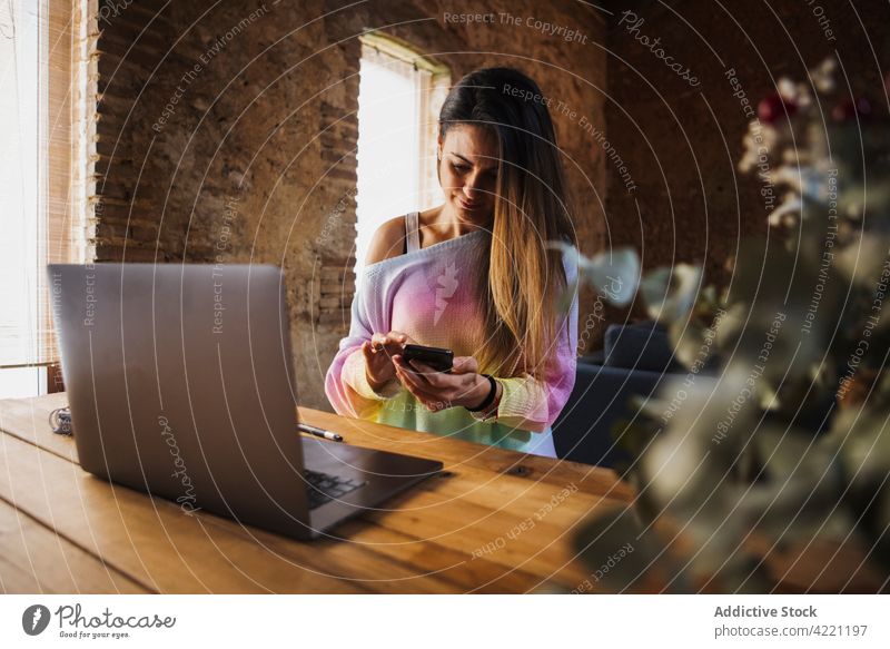 Freiberufler, der am Tisch mit Laptop zu Hause mit seinem Smartphone chattet Arbeiter plaudernd freiberuflich selbständig Loft heimwärts Frau benutzend