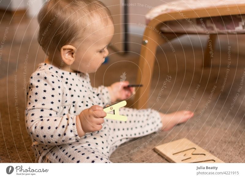 Zehn Monate altes Kleinkind spielt mit einem hölzernen Buchstabenpuzzle auf dem Boden Geduldsspiel Kind Feinmotor Fähigkeiten Zange 10 Monate alt Baby jung