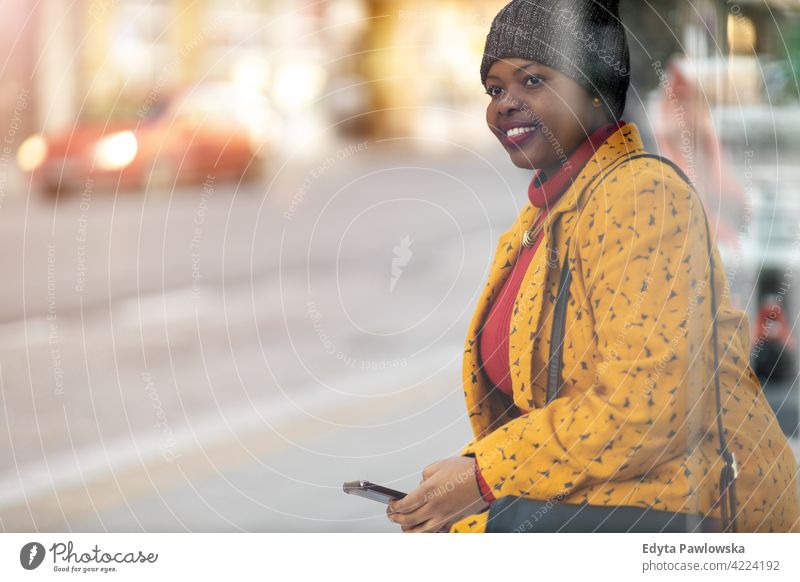 Glückliche junge Frau wartet an der Bushaltestelle Beteiligung Handy Smartphone Technik & Technologie benutzend Internet Drahtlos SMS Textnachrichten Texten