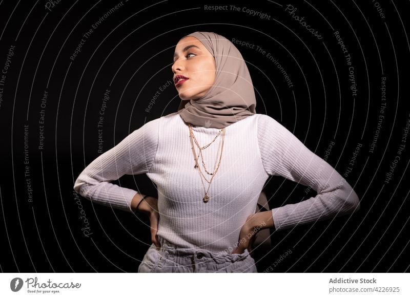 Stilvolle muslimische Frau im dunklen Studio stehend Kopftuch modisch selbstbewusst Vorschein Outfit Kopfschmuck Kleidungsstück Körperhaltung Kultur Model jung