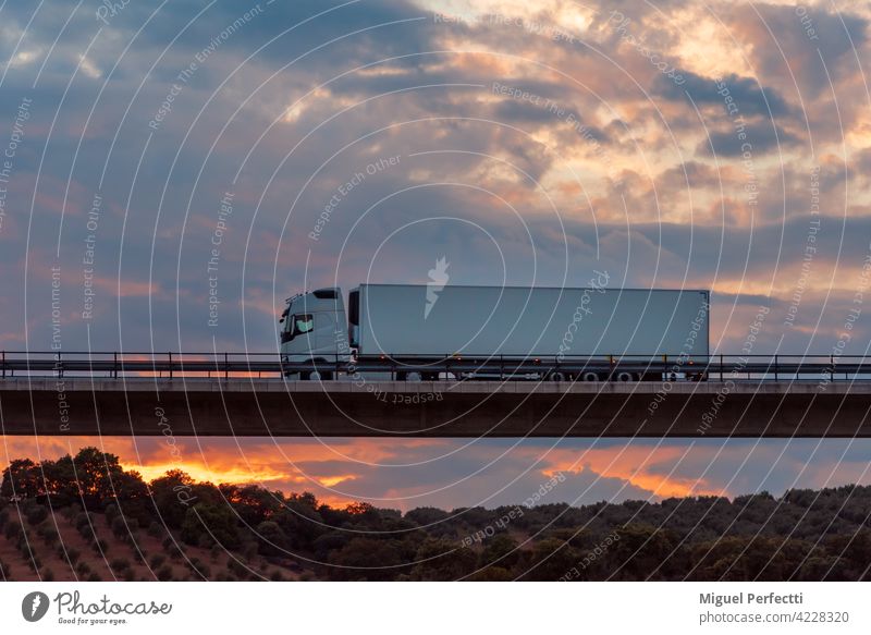 Kühltransporter, der über eine Brücke mit einem dramatischen Himmel im Hintergrund fährt. Straße Lastwagen Anhänger Transport gekühlt Sonnenuntergang Viadukt