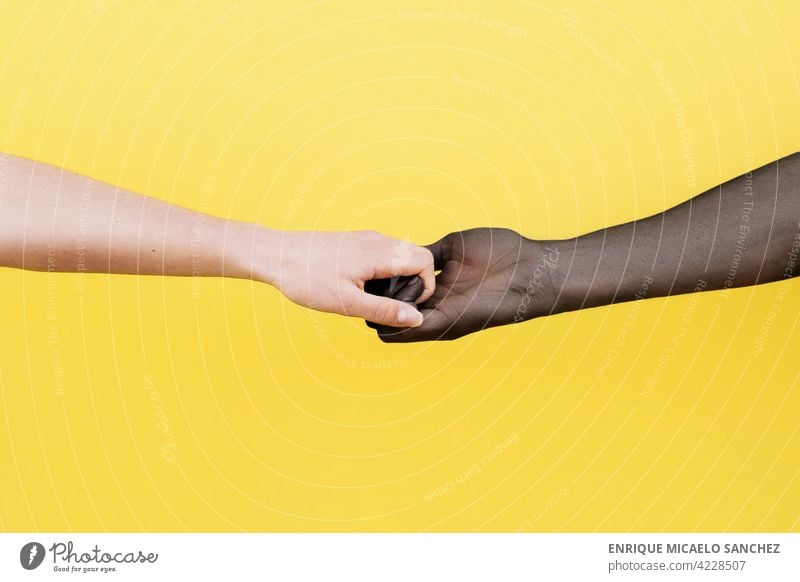 Weiße Hand und schwarze Hand umklammert auf gelbem Hintergrund Menschen Freundschaft Zusammensein Afrikanisch international Partnerschaft Haut Einheit