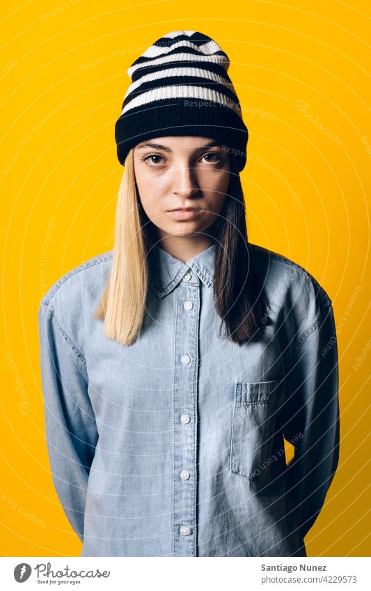 Serious Girl Wearing Hat Portrait Atelier gelber Hintergrund Porträt in die Kamera schauen Ausdruck farbenfroh Frisur lässig jung Mädchen Frau ernst