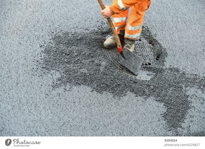 Straßenbauarbeiter mit orangener Arbeitsbekleidung und Schaufel strassenarbeiter schaufel hose reflektierend arbeiten kanaldeckel asphaltarbeiten sanieren