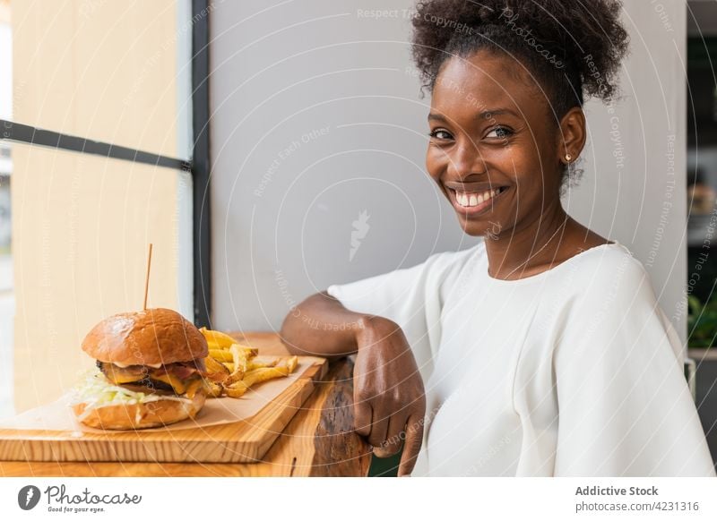 Schwarze Frau genießt Pommes und Burger in einem Restaurant essen Hamburger Fries genießen appetitlich lecker Fastfood Glaswand geschmackvoll Mahlzeit Junk Food