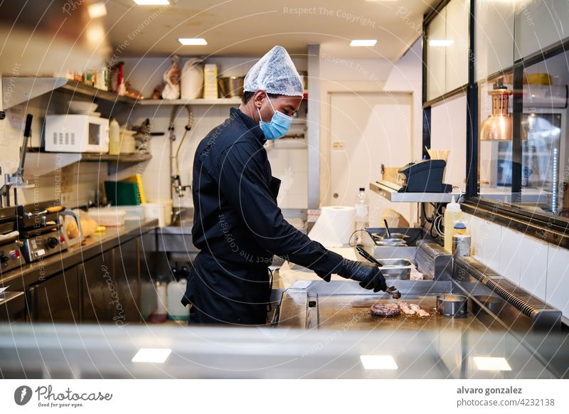 Nahaufnahme von professionellen lateinischen Koch Mann trägt eine Schutzmaske und Uniform bei der Arbeit im Restaurant Küche. Chef Kocher schützend Mundschutz