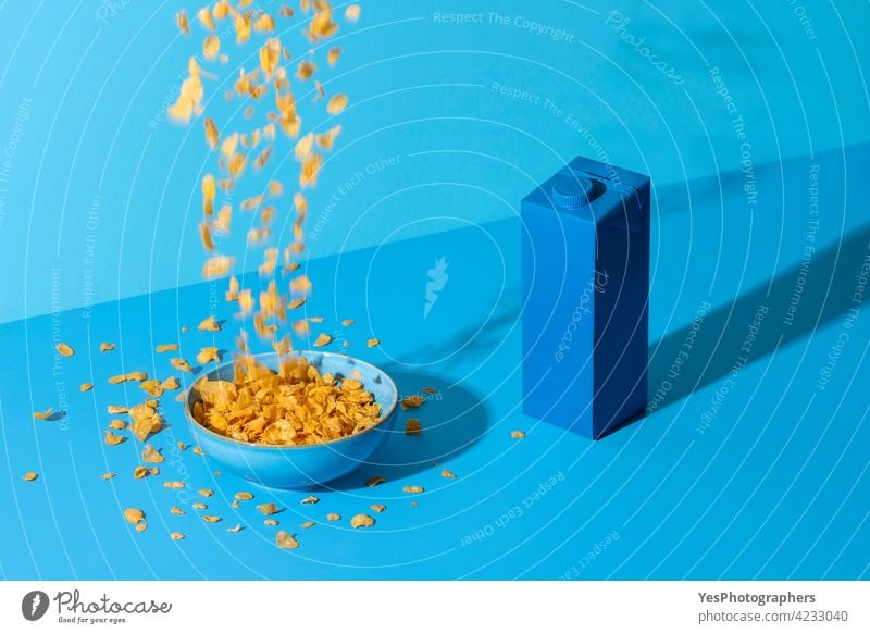 Pouring Cornflakes Müsli in einer Schüssel auf einem blauen Tisch. Frühstückstisch in natürlichem Licht. abstrakt Unfall Hintergrund Flasche Schalen & Schüsseln