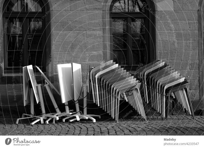 Gestapelte Designerstühle und zusammengeklappte Tische vor einem alten Café auf dem Römerberg in Frankfurt am Main in Hessen, fotografiert in neorealistischem Schwarzweiß