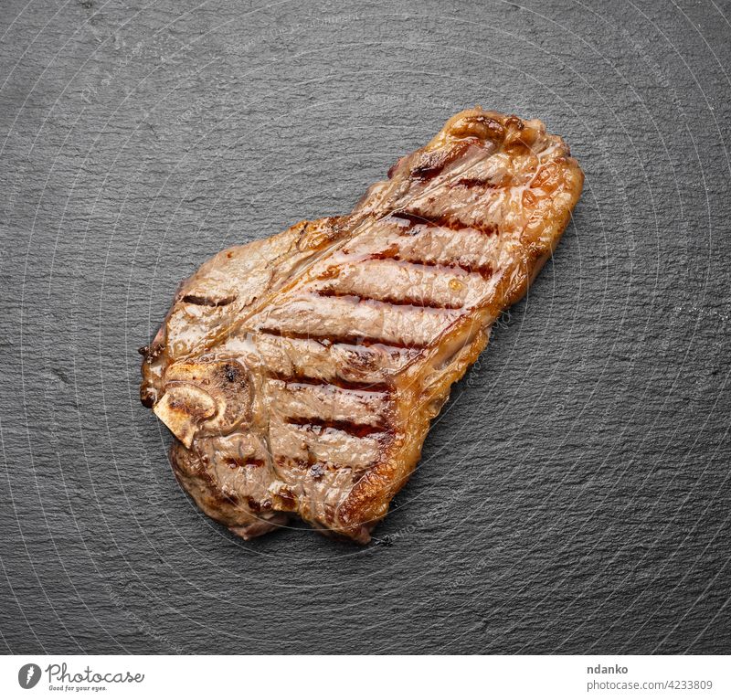 ganzes gebratenes New Yorker Rindersteak auf einem schwarzen Brett, Striploin-Doneness rare oben Barbecue grillen Rindfleisch blutig Holzplatte braun gekocht