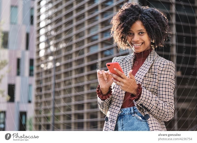 Geschäftsfrau beim Senden von Nachrichten auf ihrem Telefon. Business Frau Afro-Look Mobile finanziell Revier Großstadt urban im Freien professionell Straße