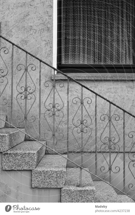Spießeridylle mit Treppengeländer aus Schmiedeeisen und Gardinen hinter dem Fenster eines Wohnhaus in Oerlinghausen bei Bielefeld im Teutoburger Wald in Ostwestfalen-Lippe, fotografiert in klassischem Schwarzweiß