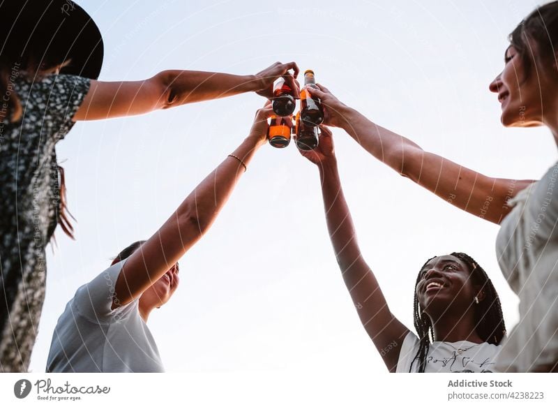 Gesellschaft von multirassischen Freundinnen, die bei Sonnenuntergang im Park auf Flaschen anstoßen Klirren Frauen Unternehmen Sommer Bier Kälte Spaß haben