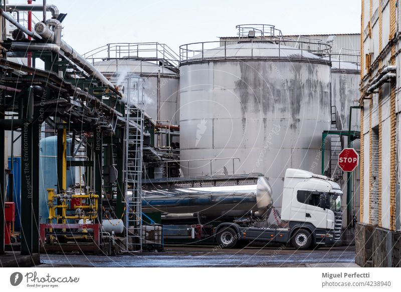 Tankwagenbeladung in einer Fabrik neben einigen Tanks und unter Rohren, die Dampf absondern. Lager Industrie Erdöl Lastwagen Pfand laden Pflanze industriell