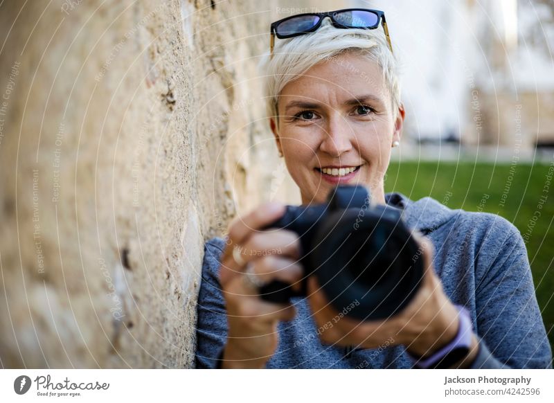 Lächelnde Frau mit der Digitalkamera in ihren Händen Porträt Fotograf Fotokamera alt Textfreiraum Kapuzenpulli Brille positiv Mädchenfotograf Fotografieren