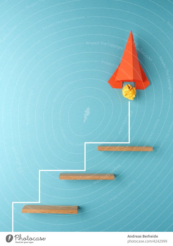 Orangefarbene Rakete oder Raumschiff, das die Treppe hinaufsteigt, Aufschwung oder Startup-Konzept zerknittert Papier Ball Inbetriebnahme Aktion Tor Erfolg