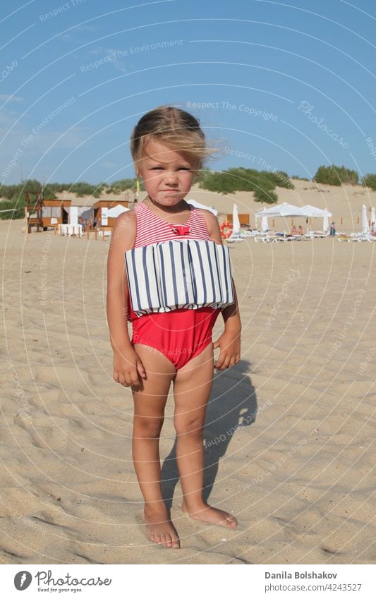 kleines Mädchen steht am Strand in einem speziellen Badeanzug für Kinder, die nicht schwimmen können. Kind im Badeanzug, den er über Wasser hielt Porträt