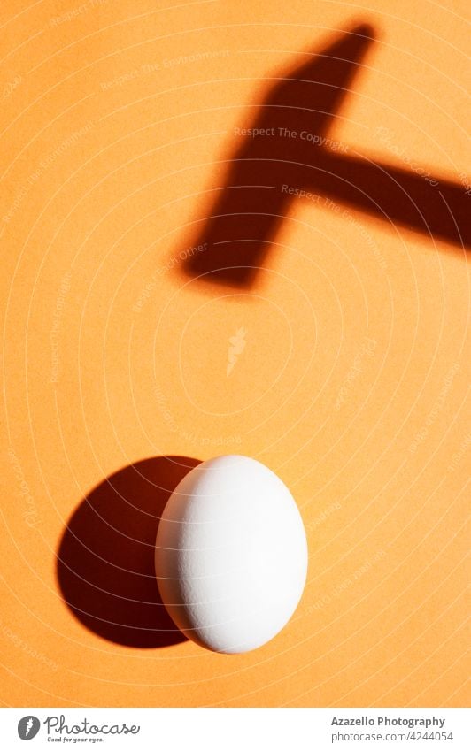Minimal-Konzept mit einem Ei unter dem harten Licht und einem Hammer Schatten auf einem orangefarbenen Hintergrund Gesundheit Tapete Leben rau schwarz