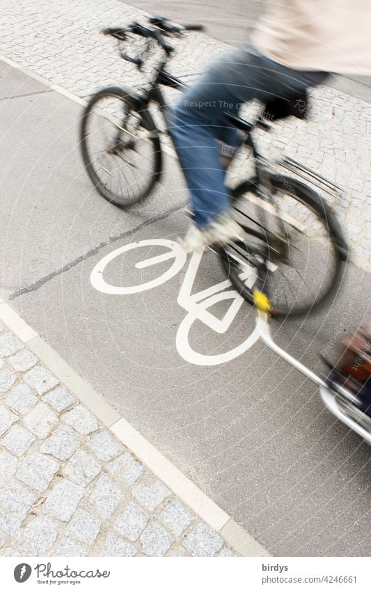 schnell vorbeifahrender Radfahrer mit Anhänger auf einem schmalen Radweg in der Stadt, Bewegungsunschärfe Radfahren Radwegsymbol Fahrradfahren Transport
