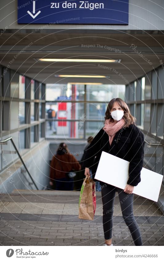 schlanke junge Frau mit FFP2-Maske  und Gepäck auf dem Bahnhof. Zugreisende Corona-Virus Mundschutz Schützen COVID-19 ÖPNV Züge Pfeil Schilder & Markierungen