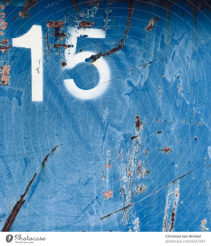 Eine weiße 15 auf der zerkratzten Metallwand eines viel genutzten alten blauen Containers Nummer Fünfzehn Zahl Ziffer Ziffern & Zahlen Metallfassade