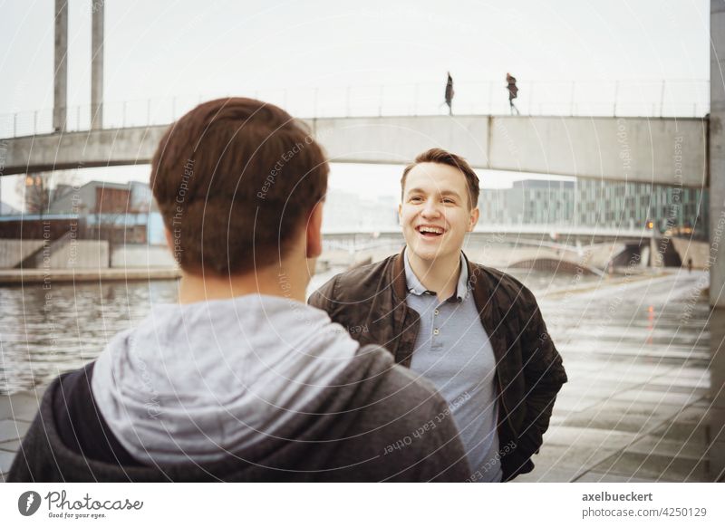 zwei männliche Teenager Freunde, die ein lustiges Gespräch am Fluss führen reden unterhalten Lachen Spaß authentisch Lifestyle echte Menschen Jugendliche Mann