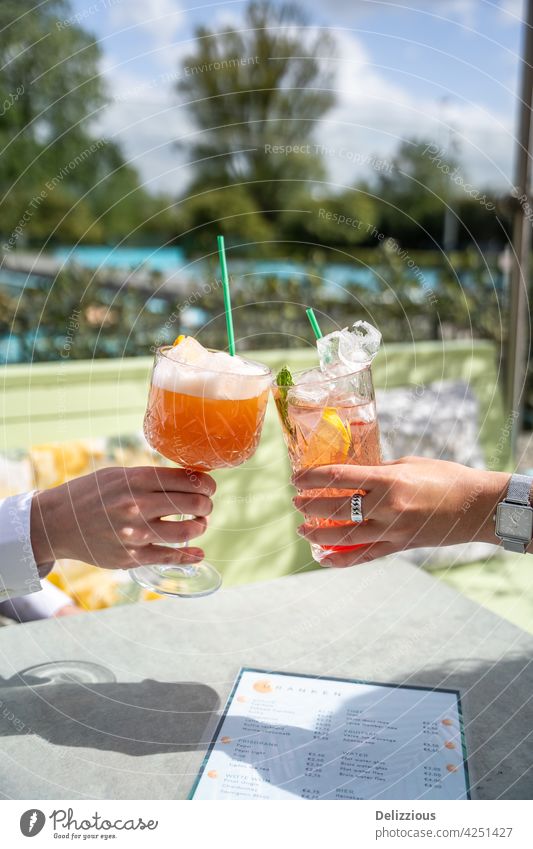 Zwei Menschen jubeln mit rosa Cocktails draußen auf einer Terrasse an einem sonnigen Tag mit Schwimmbad im Hintergrund jubelt Hände trinken Essen und Trinken