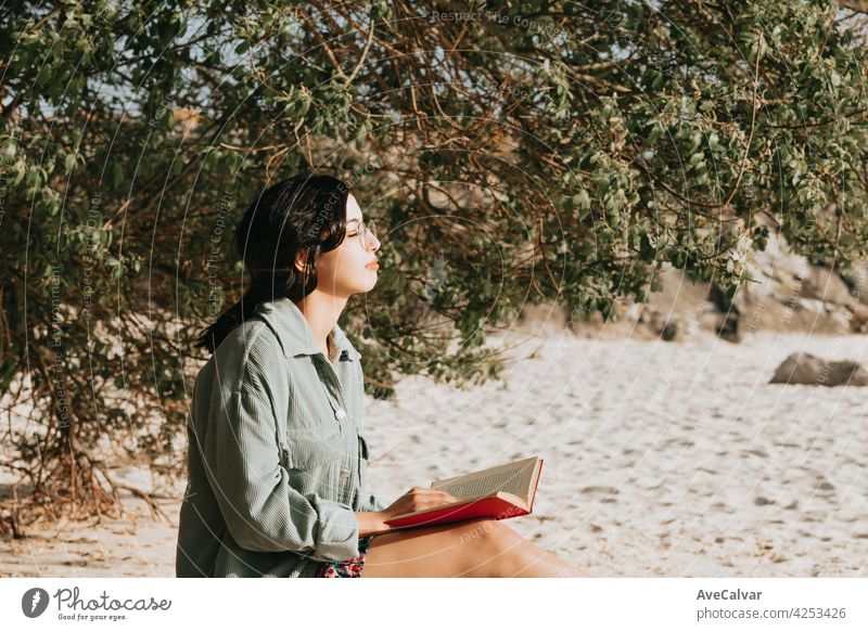 Junge marokkanische Frau auf moderne Kleidung sitzt am Strand lesen ein Buch während eines sonnigen Tages mit Kopie Raum inspirierend und entspannen Thema mit bunten Tönen