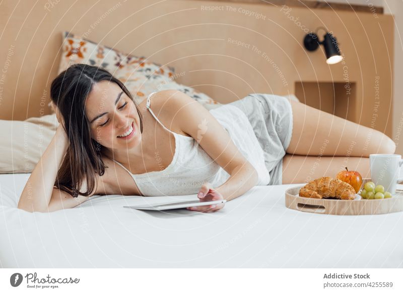 Frau mit Frühstück, die auf dem Bett chillt und ein Tablet benutzt Morgen Kälte Tablette benutzend sich[Akk] entspannen Windstille Browsen soziale Netzwerke