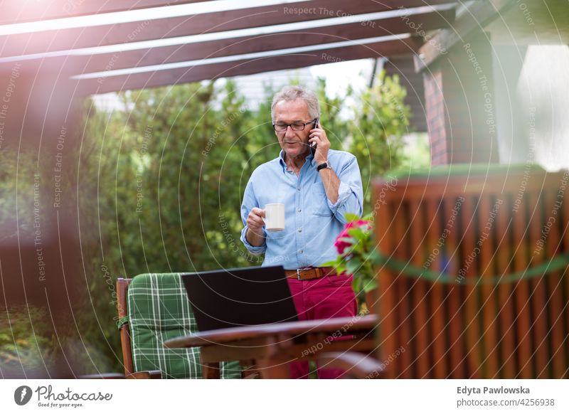 Älterer Mann benutzt Mobiltelefon im Hinterhof Senior alt Männer männlich heimwärts Haus Menschen Lifestyle genießend zu Hause häusliches Leben echte Menschen