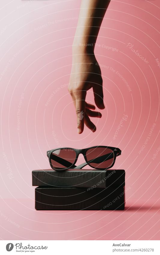 Hand erreicht eine Sonnenbrille über einen pastellrosa Hintergrund mit Kopierraum minimales Konzept stylisch Rahmen Kunststoff modern Hipster sehr wenige
