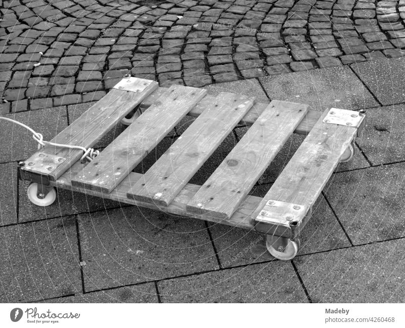 Angeleinte Holzpalette mit Rollen für den Transport von Kisten auf dem Wochenmarkt an der Bockenheimer Warte in Frankfurt am Main in Hessen, fotografiert in neorealistischem Schwarzweiß