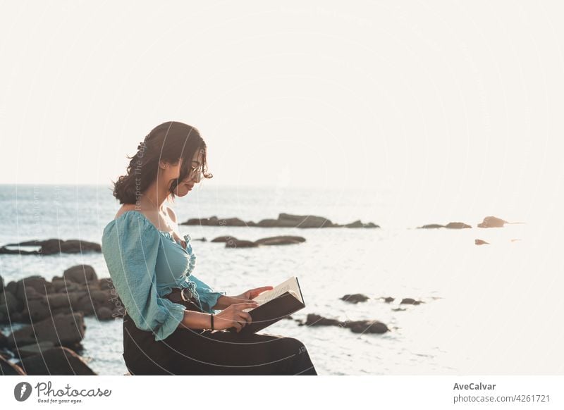 Junge Frau lächelnd in die Kamera beim Lesen am Strand während einer super Sonnenuntergang, während mit einer Maske entspannen und inspirierende Konzepte mit Kopie Raum Lebensstil bunt