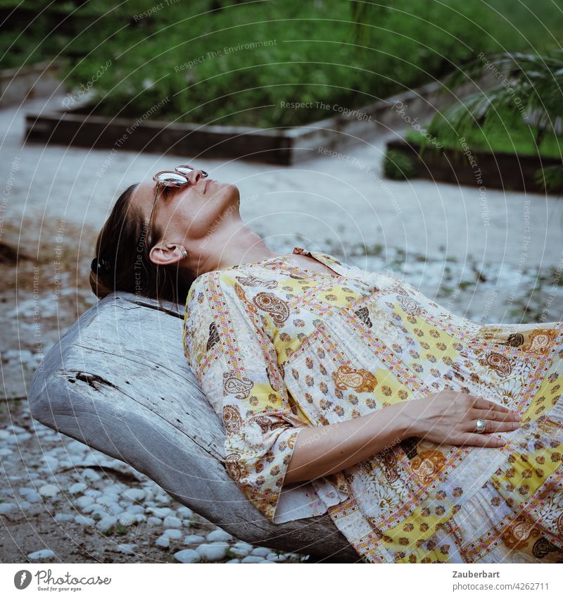 Frau im Kleid liegt entspannt auf einer Holzliege in einem Garten schön liegen entspannen Liege Urlaub chillen relaxen Sommer Reise Gemüsebeet Pflanzen grün