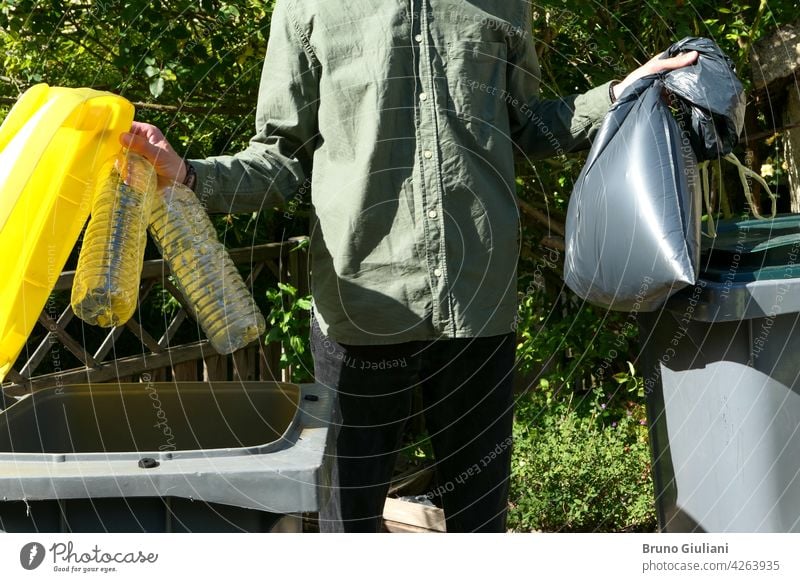 Eine Person, die eine selektive Sortierung von Hausmüll in Recycling-Behältern durchführt. Mann, der Plastikflaschen in einen gelben Behälter und Müll in einem Sack in einen grünen Behälter wirft.
