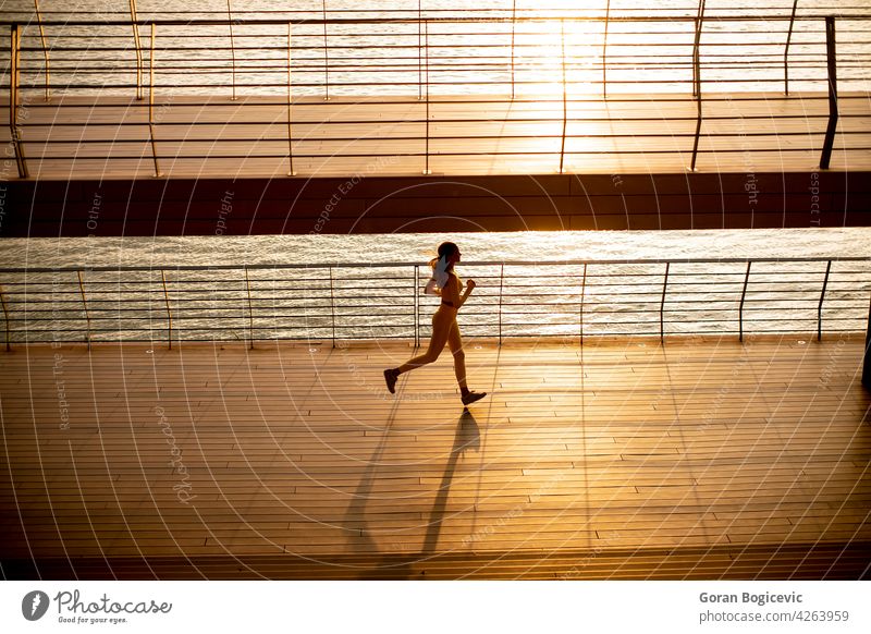 Junge Frau beim Lauftraining an der Flusspromenade jung Joggen gelb Training rennen Athlet Menschen Lifestyle Spazierweg Gesundheit Person Erwachsener Sport