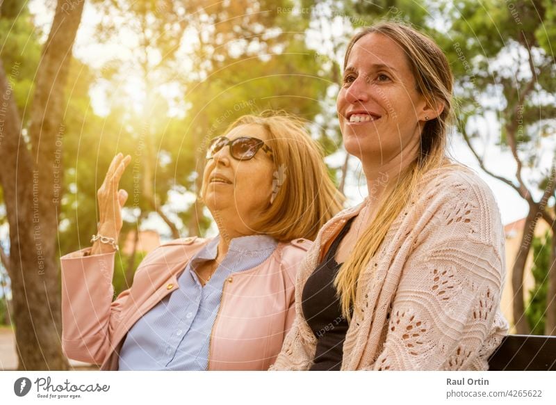Ältere Mutter und ihre erwachsene Tochter reden und genießen die Zeit zusammen in der Natur Park bei Sonnenuntergang. Frauen Glück Familie jung alt sprechend