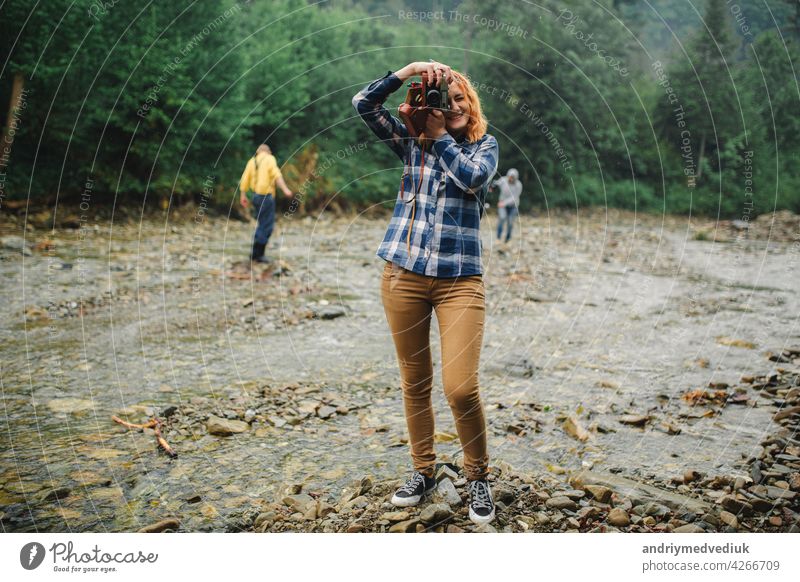 Junge rothaarige Frau mit Vintage-Kamera nimmt Foto in der Nähe des Flusses in einem Gebirge Fotokamera reisen retro jung schön Sommer Natur Fotograf Mädchen