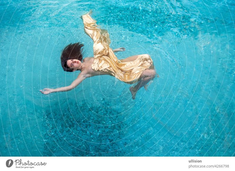 schöne sexy junge Frau Meerjungfrau in goldenen Kleid, Tuch schwimmt schwerelos elegant in der blauen türkisfarbenen Spa-Pool Wasser verträumt fliegend