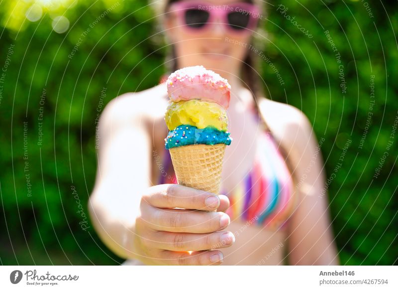 junge Frau in Regenbogen farbige Badebekleidung geben Eis, zwei bunte verschiedene Geschmacksrichtungen Eis in der Hand mit Streuseln im Sommer, Lebensmittel, Frühling, Urlaub, Urlaub Konzept