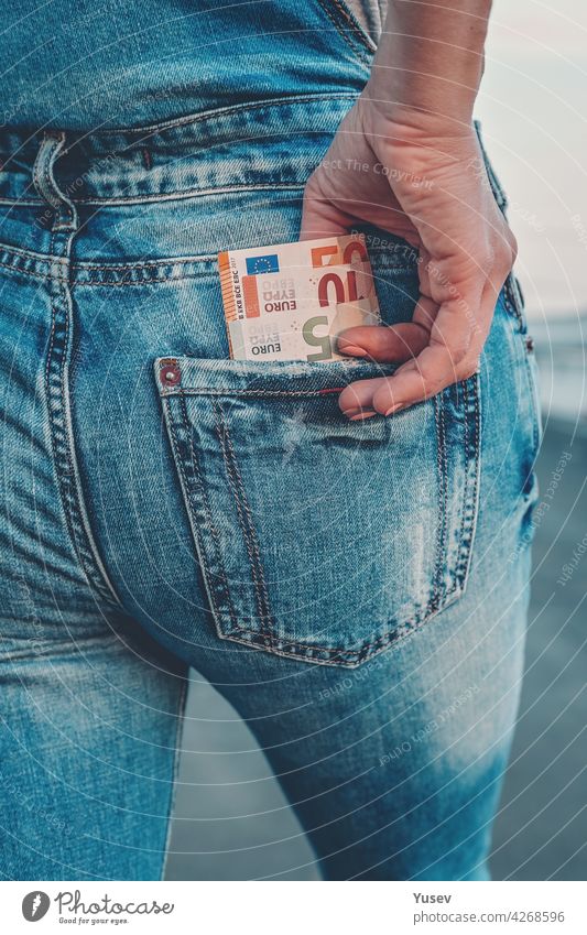 Die Hand einer Frau holt Euroscheine aus der Gesäßtasche ihrer Jeans. Das Konzept der Finanzen, Ersparnisse, finanzielle Ausgaben. Nahaufnahme unter Rechnung