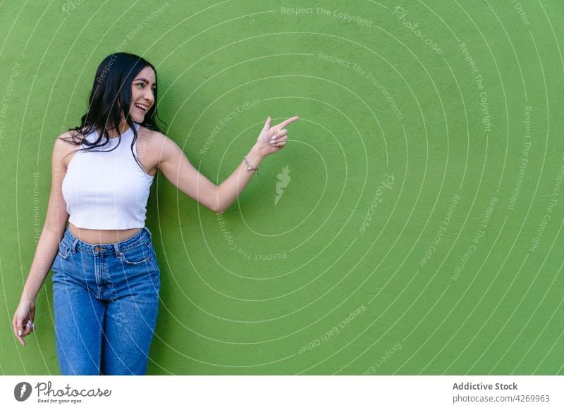 Fröhlicher Teenager, der mit dem Finger auf einen grünen Hintergrund zeigt Punkt heiter feminin freundlich angenehm charmant lässig Stil offen genießen zeigen