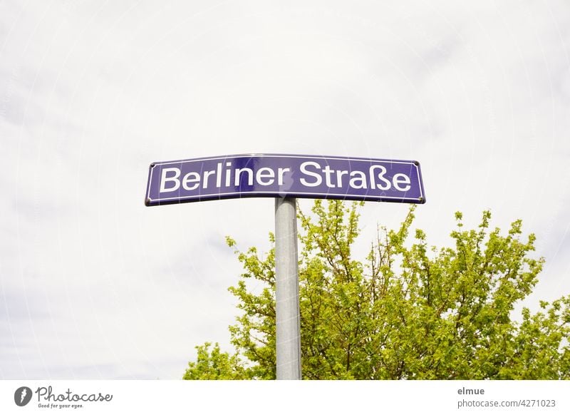 geknicktes Straßennamenschild " Berliner Straße " vor einem grünen Busch und Wolkenhimmel Straßenschild Orientierung Knick beschädigt wohnen bewölkt zentral