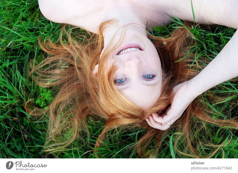 lächelndes Porträt einer schönen jungen sexy rothaarigen Frau, die rote Haare fächerförmig ausbreitet und entspannt auf dem grünen Gras liegt, auf dem Kopf stehend, Kopierraum