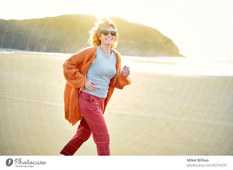 Junge reife blonde kaukasische Frau läuft im Freien in einem Strand in einem sonnigen Tag.  Lifestyle-Konzept. Porträt Wellness Frauen Gesundheit freudig rennen