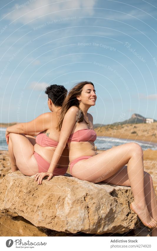 Frauen in Badeanzügen auf Felsbrocken am Strand in der Nähe des Ozeans Sand MEER Freude Blauer Himmel Freund Badebekleidung Felsen jung Sommer Urlaub Stein Ufer