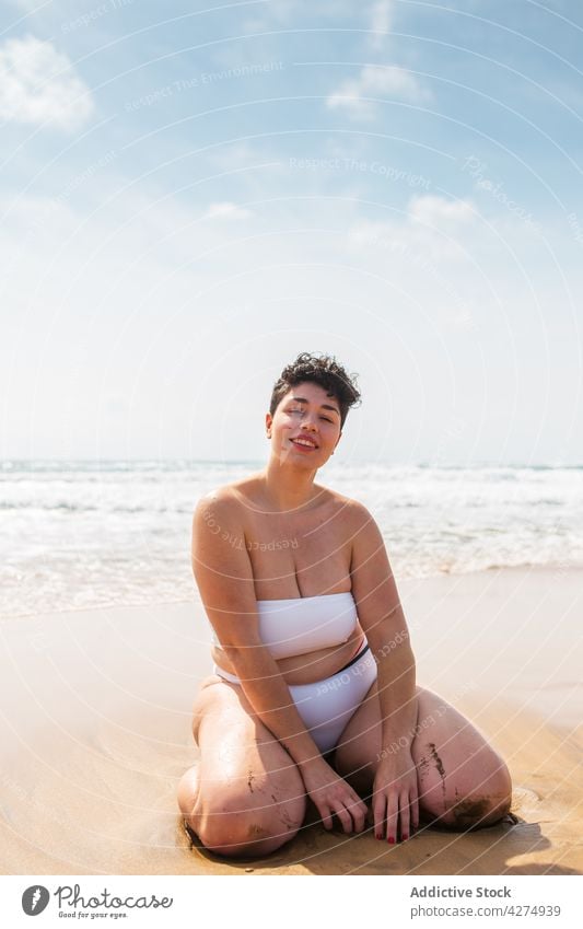 Frau sitzt am Sandstrand in der Nähe des Meeres Strand Lächeln Übergröße Badeanzug Urlaub Blauer Himmel Glück jung aqua genießen MEER allein hell Freude