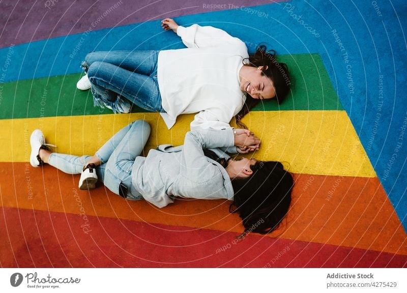 Glückliches weibliches Paar auf buntem Boden liegend und Hände haltend Frauen Spaß lgbtq Lachen Freude farbenfroh Stolz lesbisch sorgenfrei Spaß haben Lügen