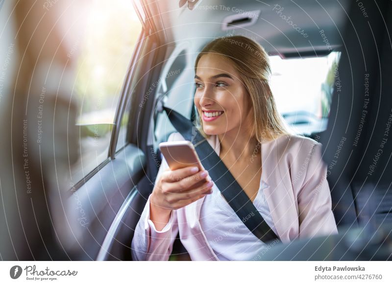 Junge Frau mit Smartphone auf dem Rücksitz eines Autos Carsharing selbstbewusst Lächeln Befriedigung attraktiv schön junger Erwachsener Freude positiv Inhalt